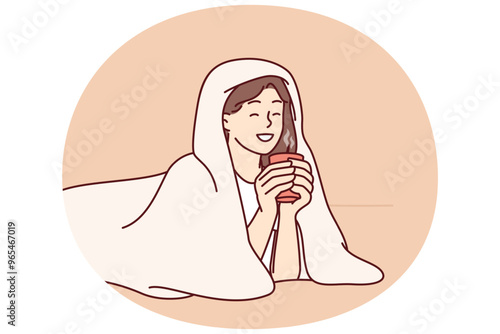Girl with cup of hot coffee lies wrapped in blanket and smiles enjoying winter morning. Woman drinking hot drink with blanket to keep warm after walking on cold street for autumn mood concept