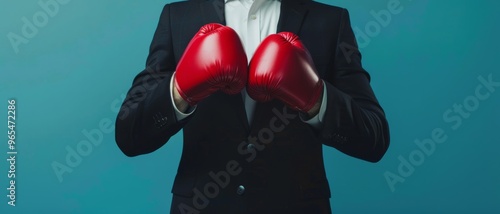 A businessperson in a dark suit poised for action, wearing red boxing gloves symbolizing readiness and competitive spirit against a blue background. photo