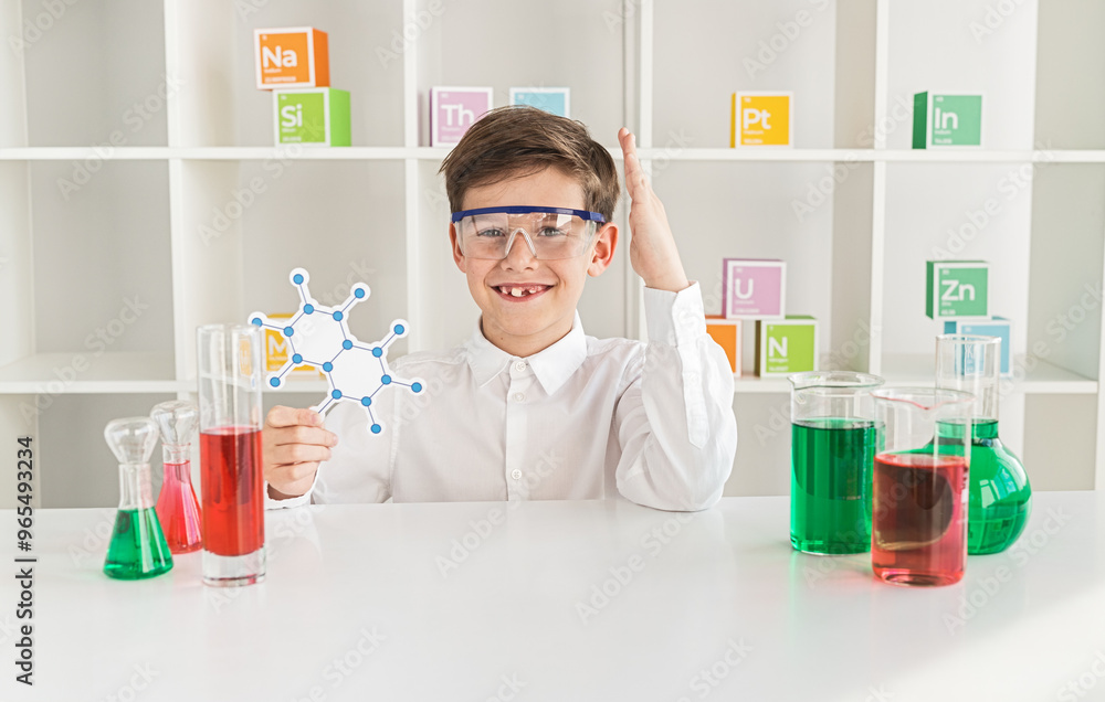 Smiling young boy wearing safety goggles in a chemistry lab, holding a molecule model. Laboratory equipment and colorful chemical solutions surround him. Smiling young boy wearing safety goggles in a chemistry lab, holding a molecule model. Laboratory equipment and colorful chemical solutions surround him.