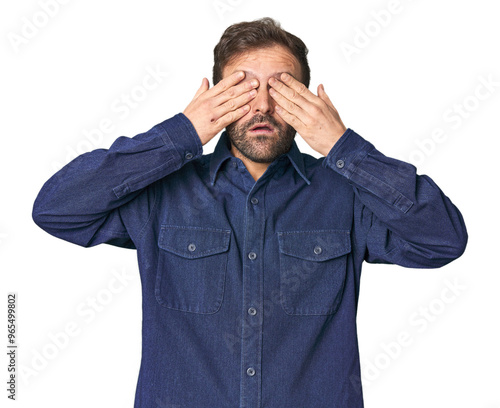 Studio portrait of young Hispanic male afraid covering eyes with hands.