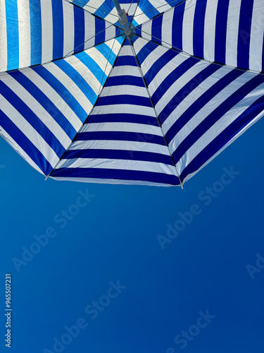 Fragment of white and blue striped beach umbrella close up against clear blue sky with text space