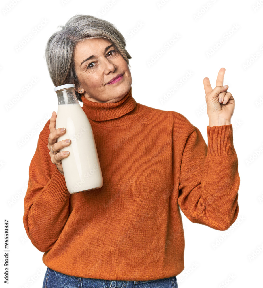 Caucasian mid-age female holding milk bottle joyful and carefree showing a peace symbol with fingers. Caucasian mid-age female holding milk bottle joyful and carefree showing a peace symbol with fingers.