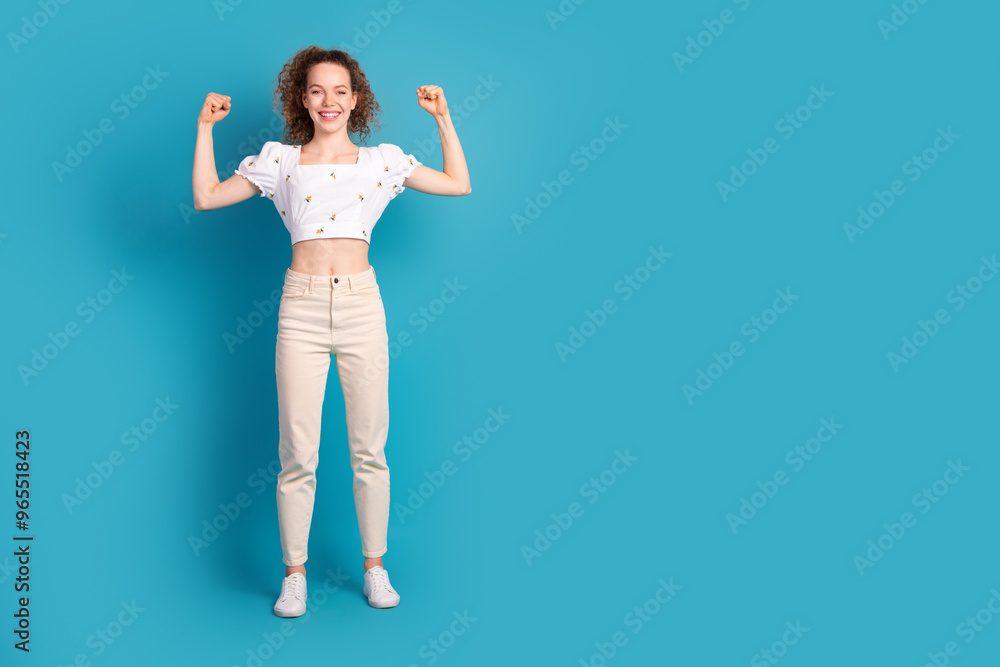 Full length photo of lovely young lady flexing muscles winning dressed stylish white garment isolated on blue color background Full length photo of lovely young lady flexing muscles winning dressed stylish white garment isolated on blue color background