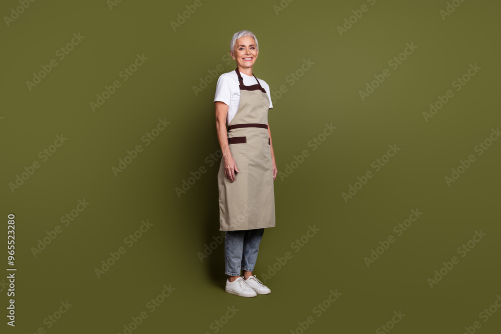 Full length photo of cheerful pretty lady dressed apron owning cafe smiling empty space isolated green color background Full length photo of cheerful pretty lady dressed apron owning cafe smiling empty space isolated green color background
