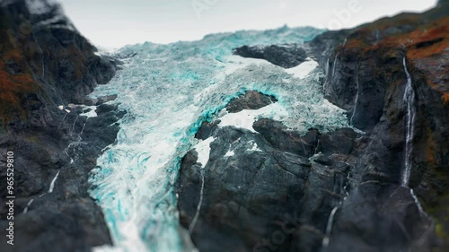 The icy expanse of a glacier cuts through a mountain valley, with streams of water flowing from its edges. A tilt-shift video. photo