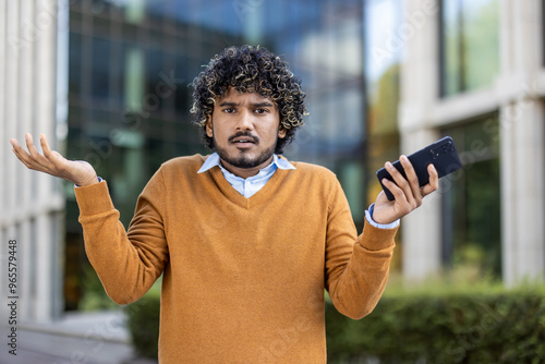 Foto Man with curly hair in sweater holding smartphone with confused expression