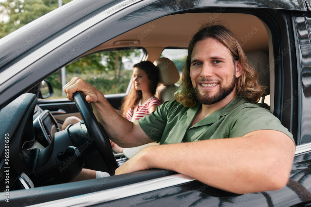 Happy young man driving a car with a woman in the passenger seat, enjoying a sunny day outdoors Happy young man driving a car with a woman in the passenger seat, enjoying a sunny day outdoors