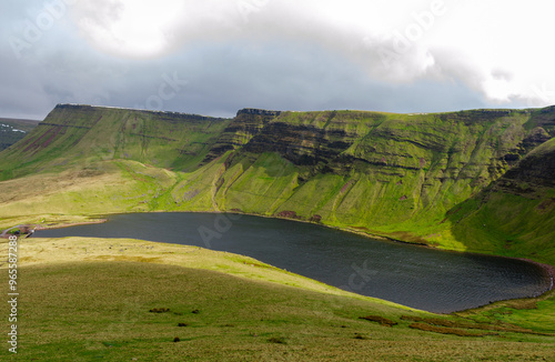 Serene landscape of a lake surrounded by green cliffs under a cloudy sky in near Buttermere in Wales.