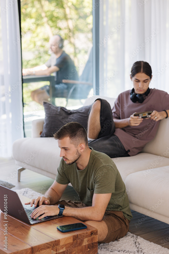 Three men using gadgets during the vacation. One sitting on floor, second on sofa and third on terrace Three men using gadgets during the vacation. One sitting on floor, second on sofa and third on terrace