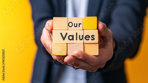 A businessman holds wooden blocks spelling "Our Core Values" against a bright yellow background. This image represents the importance of core values in business. There's room for yourmessage or text.