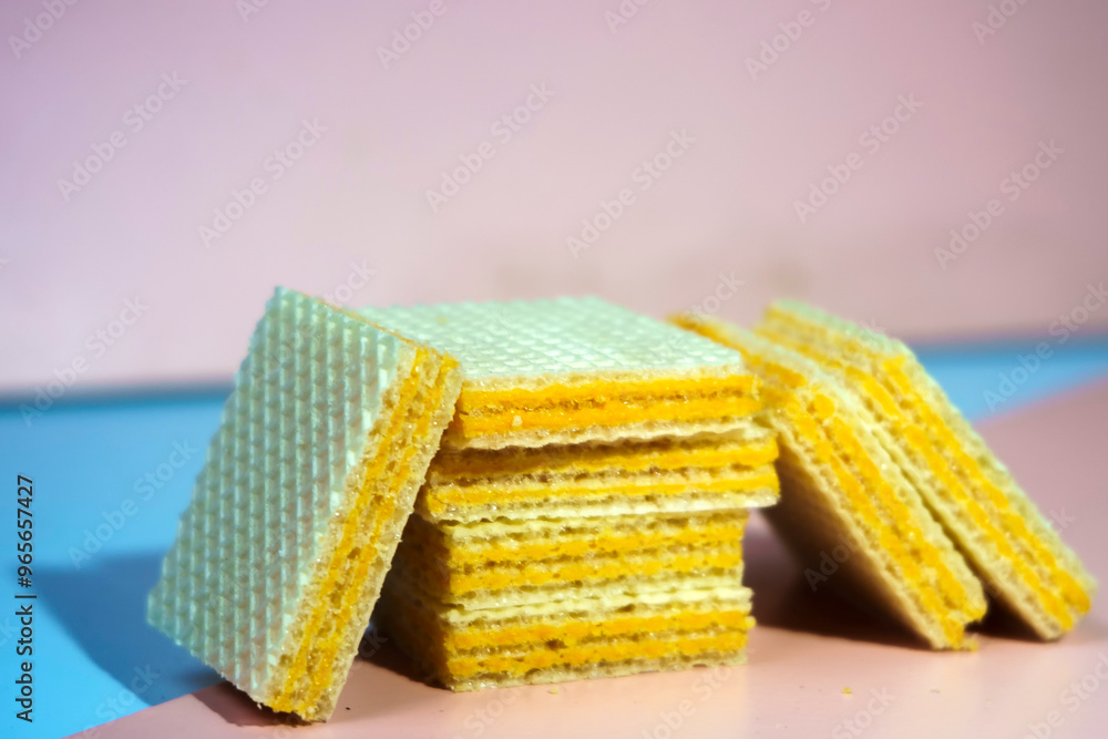 Fototapeta premium A pile of square, yellow wafers arranged on a blue and pink background.