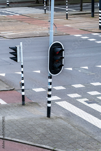 A traffic light at an empty urban intersection shows a red signal, with black and white striped poles and clearly marked crosswalks, viewed from above.