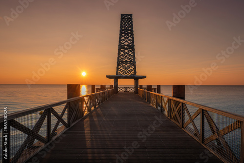 The sun appears on the left side of the horizon, tinting the top of the Pontoon, the sky of warm and orange tones. Sunrise on the Pontoon of Port Leucate, France. photo