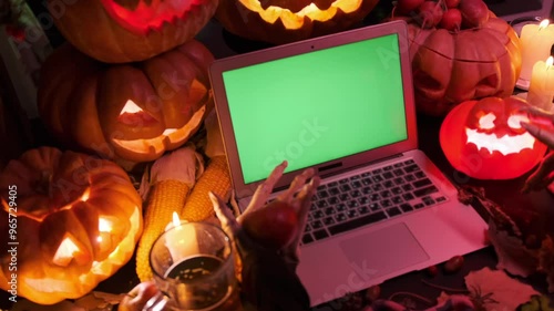 Creepy monster hands next to laptop with green screen surrounded by shimmering pumpkins jack o lanterns, halloween holiday background. photo