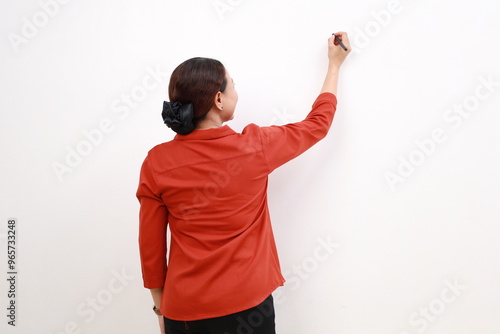 Rear view of young Asian female in red shirt writing something on board with marker