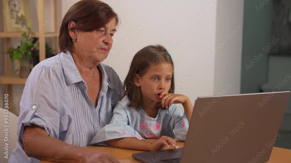 Granddaughter and grandmother using laptop together on table at home. Loving senior woman talking to girl as they share and learn from the computer Granddaughter and grandmother using laptop together on table at home. Loving senior woman talking to girl as they share and learn from the computer