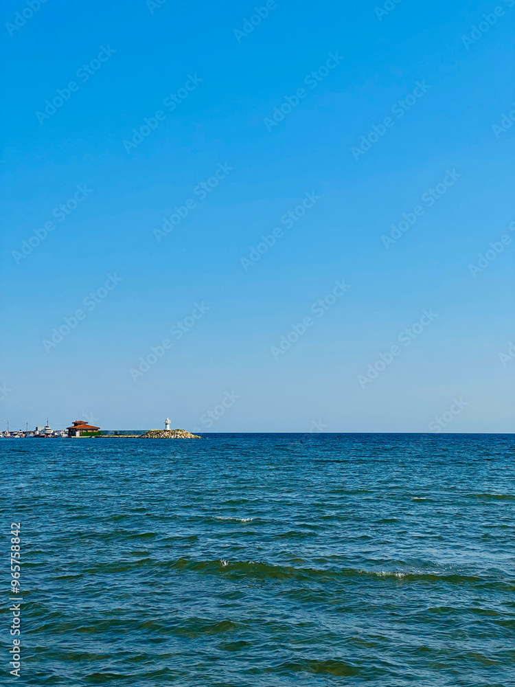 View of the sea and the lighthouse on the background of blue sky View of the sea and the lighthouse on the background of blue sky
