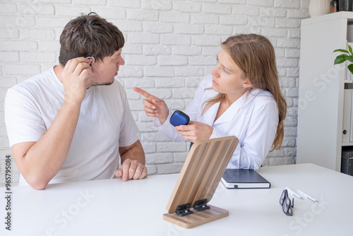 young male patient testing hearing aid in clinic exam room, female doctor helping