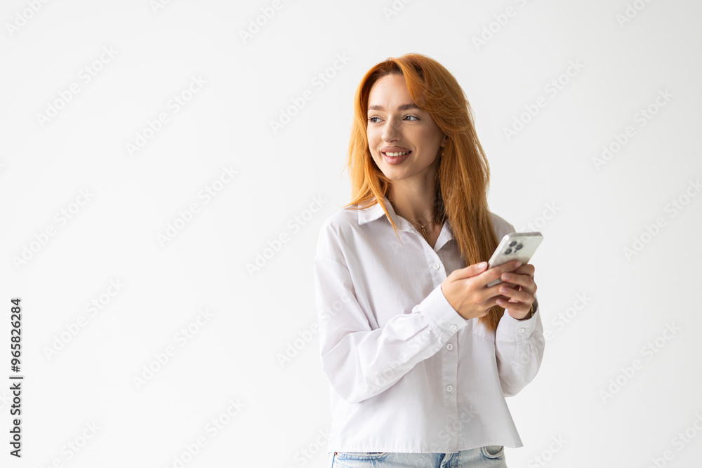 Smiling woman standing with cellphone and looking happy at camera, using mobile phone app, white background Smiling woman standing with cellphone and looking happy at camera, using mobile phone app, white background