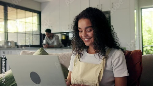 Happy woman on couch, laptop on thigh, smiling while sharing event details