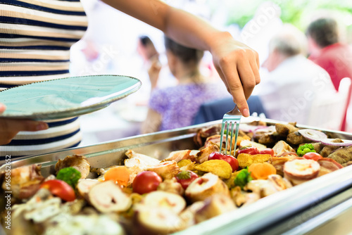 Slika na platnu A person serves delicious grilled food at a lively outdoor gathering during a su