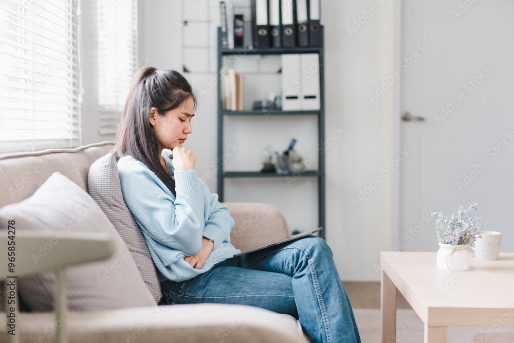 A young woman sits thoughtfully on sofa, holding phone and looking at tablet in cozy, well lit living room. atmosphere is calm and reflective, perfect for concentration. A young woman sits thoughtfully on sofa, holding phone and looking at tablet in cozy, well lit living room. atmosphere is calm and reflective, perfect for concentration.