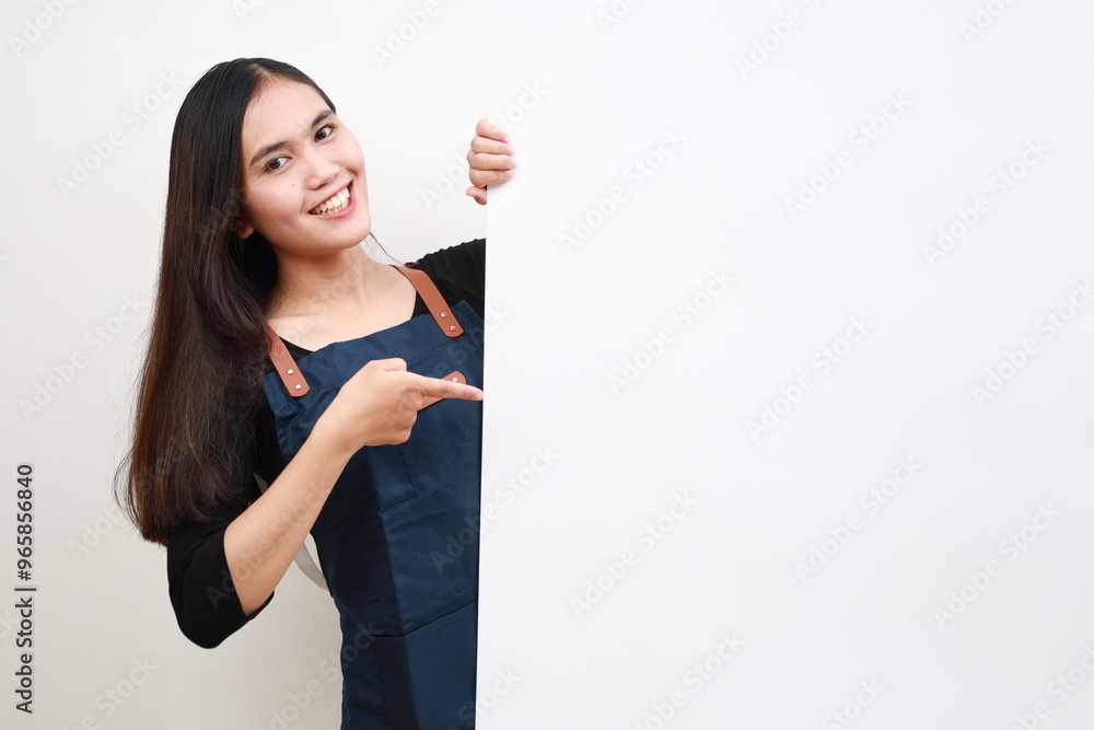 Happy Asian woman in apron pointing something on white advertisement board on white background Happy Asian woman in apron pointing something on white advertisement board on white background