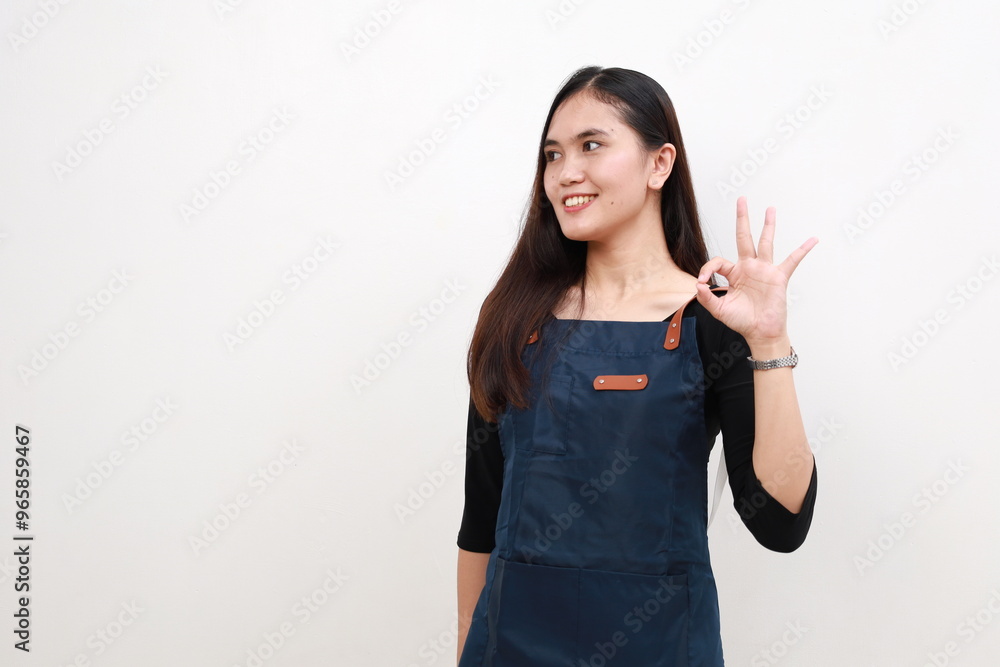 Portrait smiling young asian woman wearing apron showing making okay sign gesture with hand looking sideways isolated white background, waitress or entrepreneur, small business or startup Portrait smiling young asian woman wearing apron showing making okay sign gesture with hand looking sideways isolated white background, waitress or entrepreneur, small business or startup