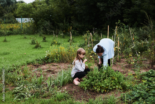 Little girl helping her mother work in the garden in the backyard of the house