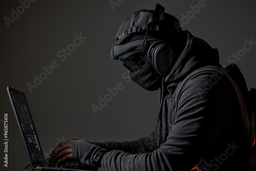 A hooded hacker with a hidden face accesses personal data on a computer in the dark. A technological, cyber crime concept. photo