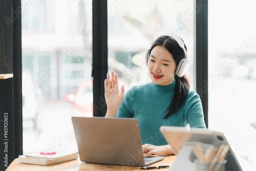 Engaged woman with headphones waving while using laptop in cafe