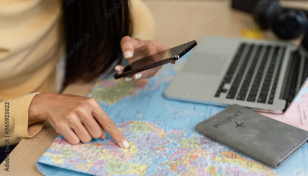 Young Woman Checking Travel Information on Smartphone with Map and Passport on Desk, Planning Vacation Trip Young Woman Checking Travel Information on Smartphone with Map and Passport on Desk, Planning Vacation Trip