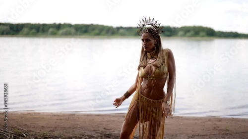 A woman in a gold suit performs a graceful dance on the shore of the lake, her movements are smooth, and the fringe on the outfit emphasizes every movement, creating a magical effect. photo