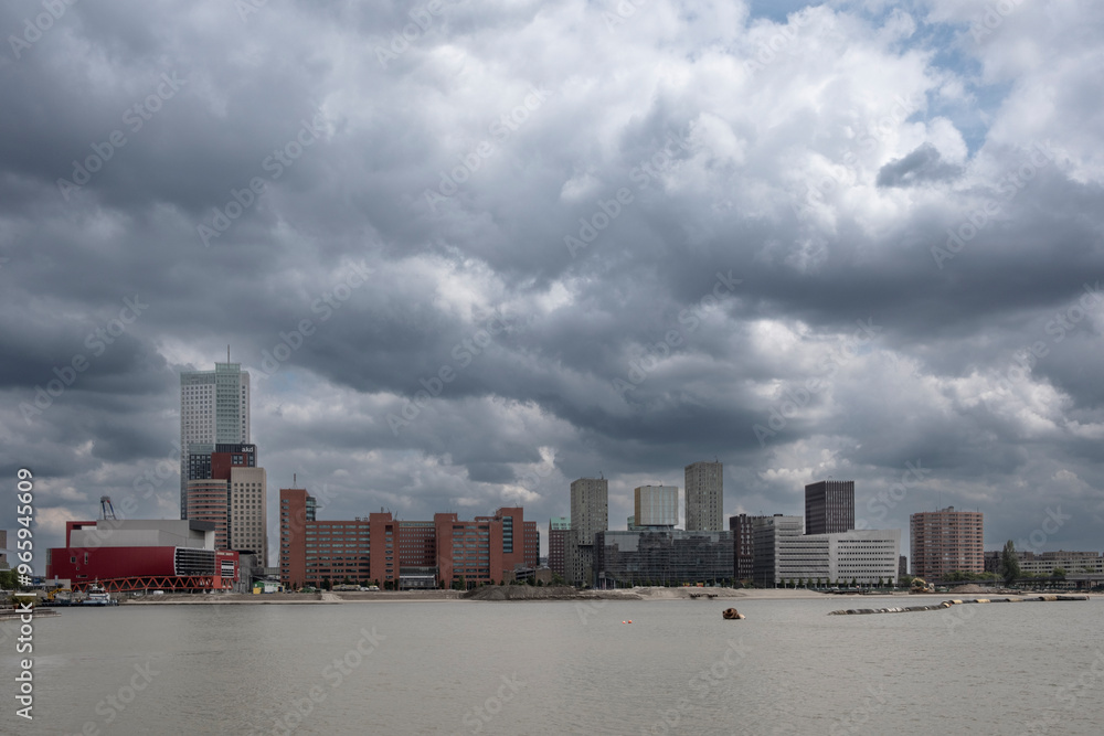 A panoramic urban waterfront view showcasing diverse high-rise towers and buildings under a dramatic cloudy sky, depicting modern city living and architectural diversity in Rotterdam