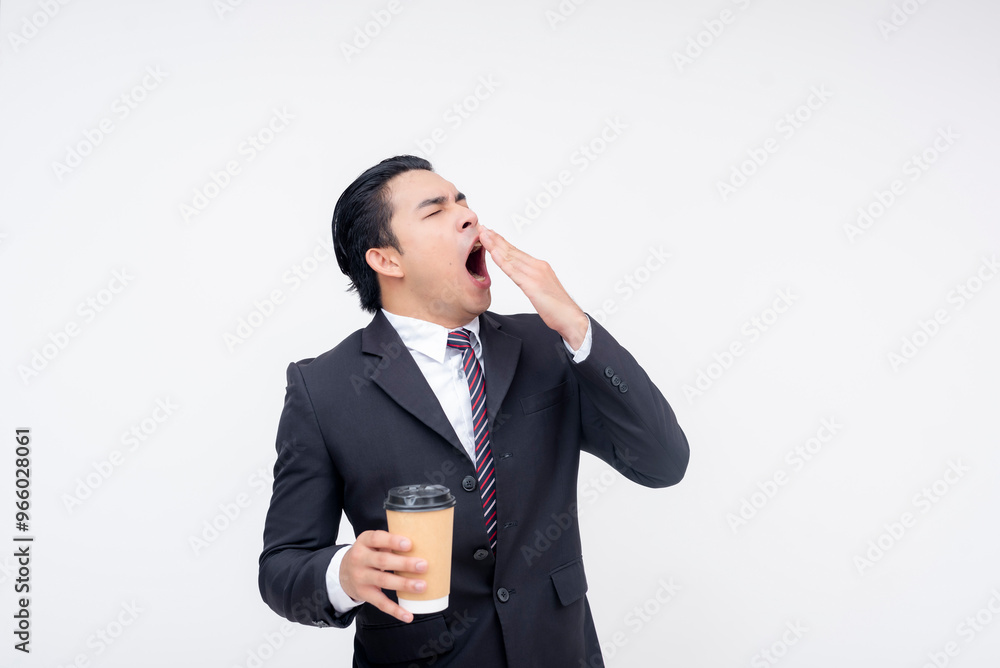 A tired young asian business executive yawning while holding a cup of coffee. Isolated on a white background. A tired young asian business executive yawning while holding a cup of coffee. Isolated on a white background.