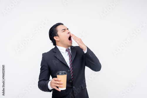 A tired young asian business executive yawning while holding a cup of coffee. Isolated on a white background. photo