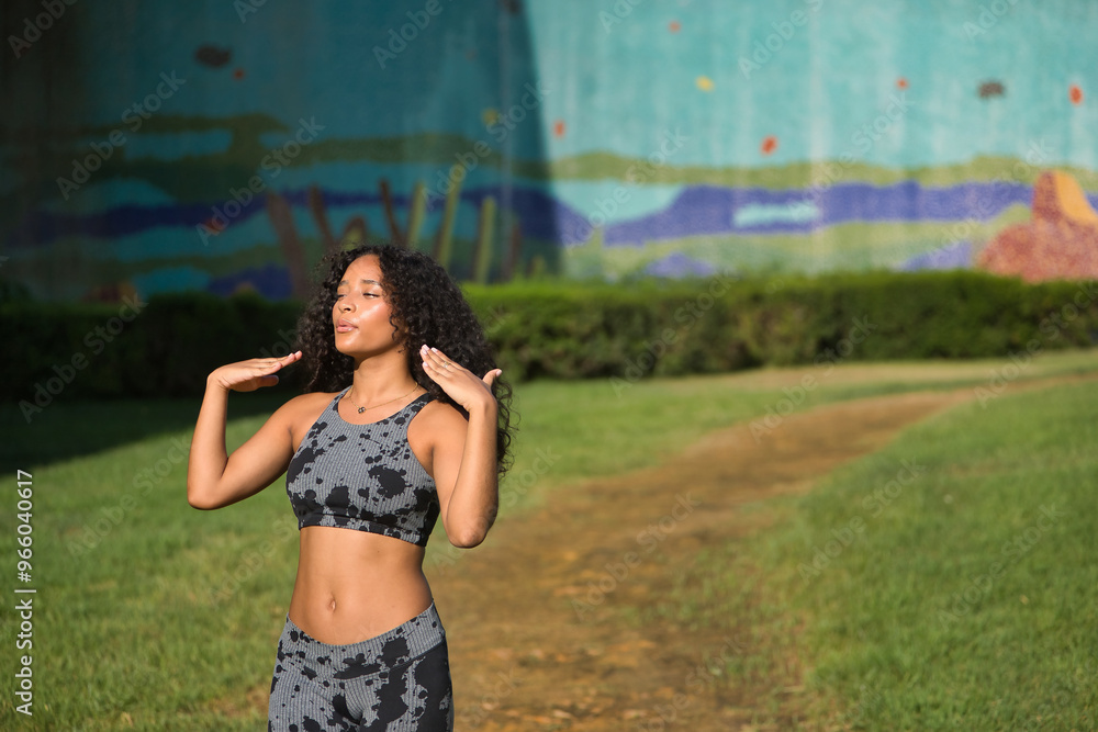 Fototapeta premium Young, pretty, brunette, Latina woman with curly hair and sports clothes, fanning herself with her hands, tired and very hot after completing her exercise routine. Concept sport, exercise, running.