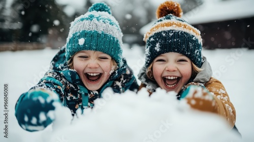 Two joyful children dressed in warm winter clothing, laughing and playing in the snow. The snowy scene captures their happiness and playful spirit during a winter day. photo