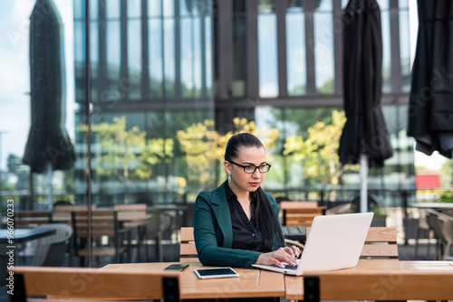 businesswoman in suit using laptop while sitting at table outside modern building on city street