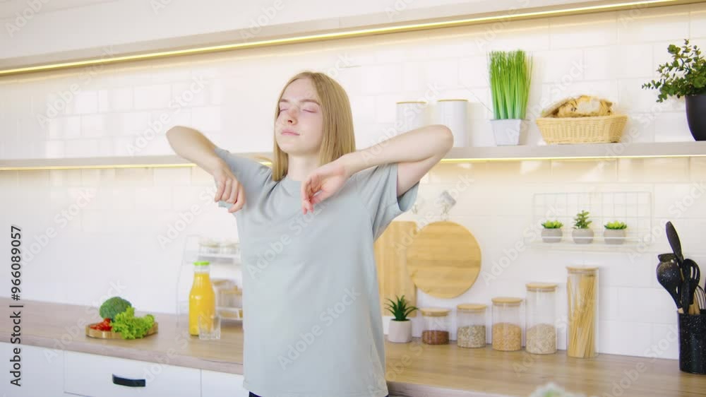 A Scandinavian blonde woman in casual home clothes enters a modern, bright kitchen, stretching and yawning after waking up, ready to start her morning routine A Scandinavian blonde woman in casual home clothes enters a modern, bright kitchen, stretching and yawning after waking up, ready to start her morning routine
