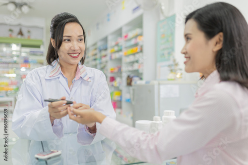Pharmacist assisting customer at pharmacy counter. Asian healthcare  smiling and providing service in drugstore. she use glucometer screening patient, keep blood exam to diabetic screening.