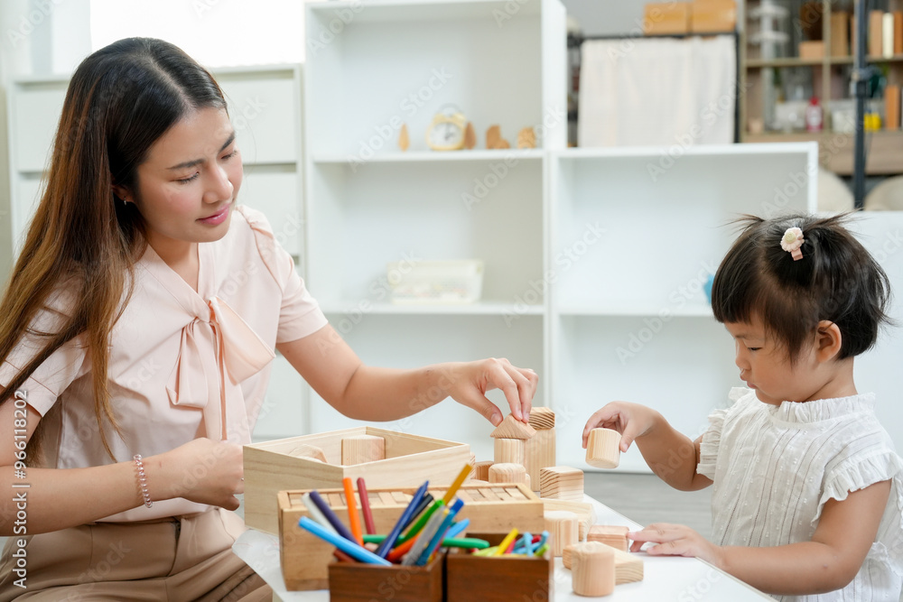 Asian woman sitting at a table playing with wooden blocks alongside toddler. early education, building motor skills and cognitive development. Calm and focused atmosphere in cozy home setting. Asian woman sitting at a table playing with wooden blocks alongside toddler. early education, building motor skills and cognitive development. Calm and focused atmosphere in cozy home setting.