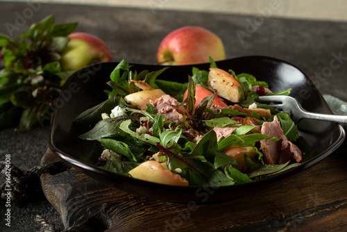 bowl of salad with duck breast, arugula and baked apples on dark table