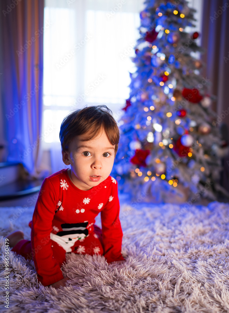Young child in red holiday sweater sits on floor by Christmas tree. A child in a festive red sweater plays on a soft rug beside a decorated Christmas tree Young child in red holiday sweater sits on floor by Christmas tree. A child in a festive red sweater plays on a soft rug beside a decorated Christmas tree