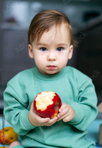 Child enjoying a fresh apple while sitting in a cozy indoor space. A young child holds a partially eaten apple, showcasing curiosity and delight