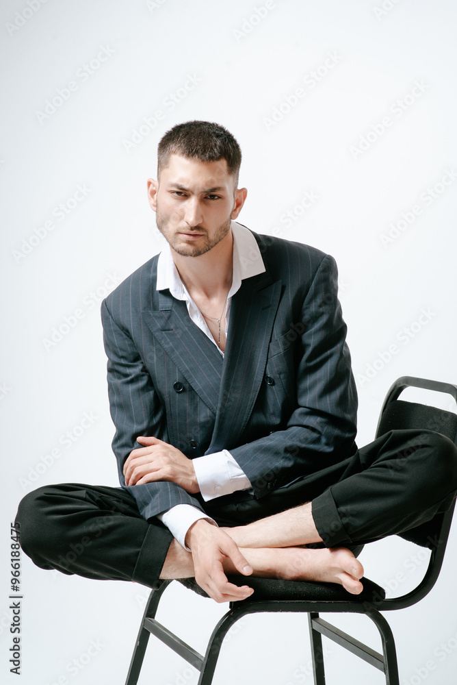 Handsome man, fashion model sits on chair barefoot Handsome man, fashion model sits on chair barefoot