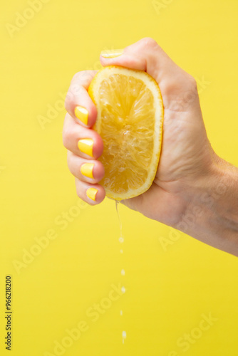 A woman's hand with yellow fingernails squeezing half a lemon.