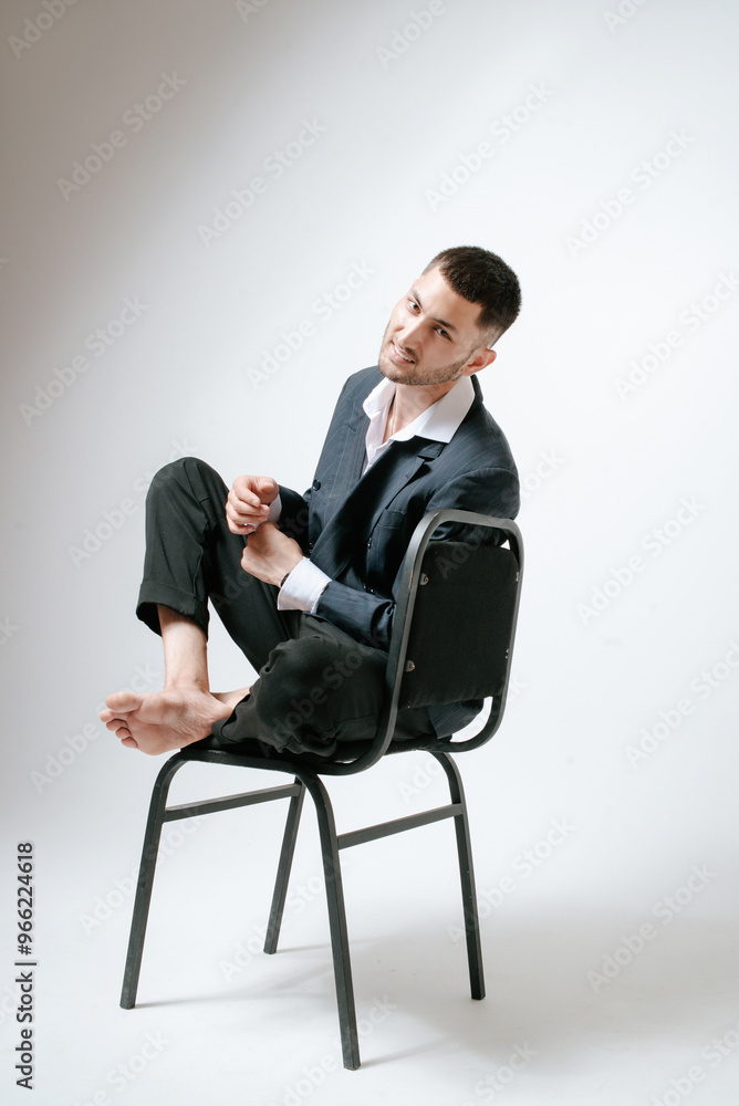 Handsome man, fashion model sits on chair barefoot Handsome man, fashion model sits on chair barefoot