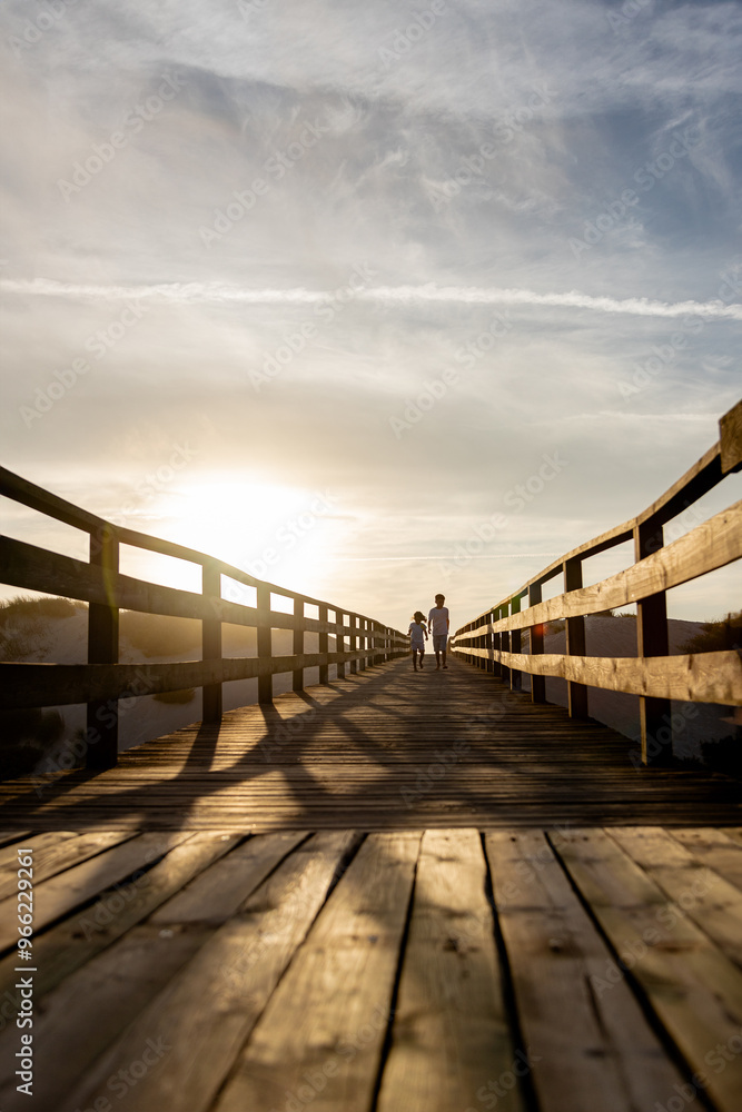 Obraz premium Two children run along a wooden boardwalk bathed in the warm glow of the sunset. Capturing the essence of freedom, adventure and the beauty of nature.