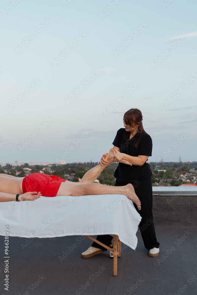 Master massage therapist on the roof of a house in the city gives a massage to a beautiful young man with a tattoo, close-up hands lubricating skin and body with oil. Medicine and procedure Master massage therapist on the roof of a house in the city gives a massage to a beautiful young man with a tattoo, close-up hands lubricating skin and body with oil. Medicine and procedure